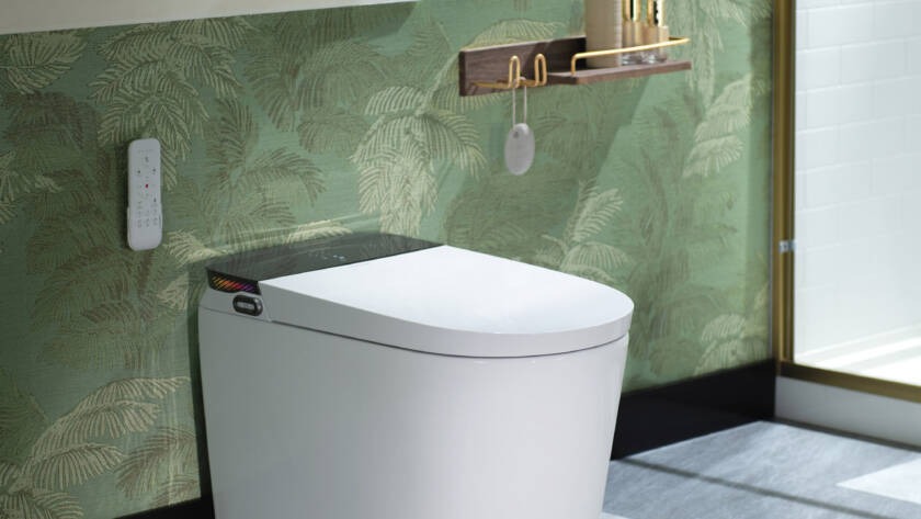 Modern smart toilet installation with remote control, featuring sleek design and tropical wallpaper in a stylish bathroom setting.