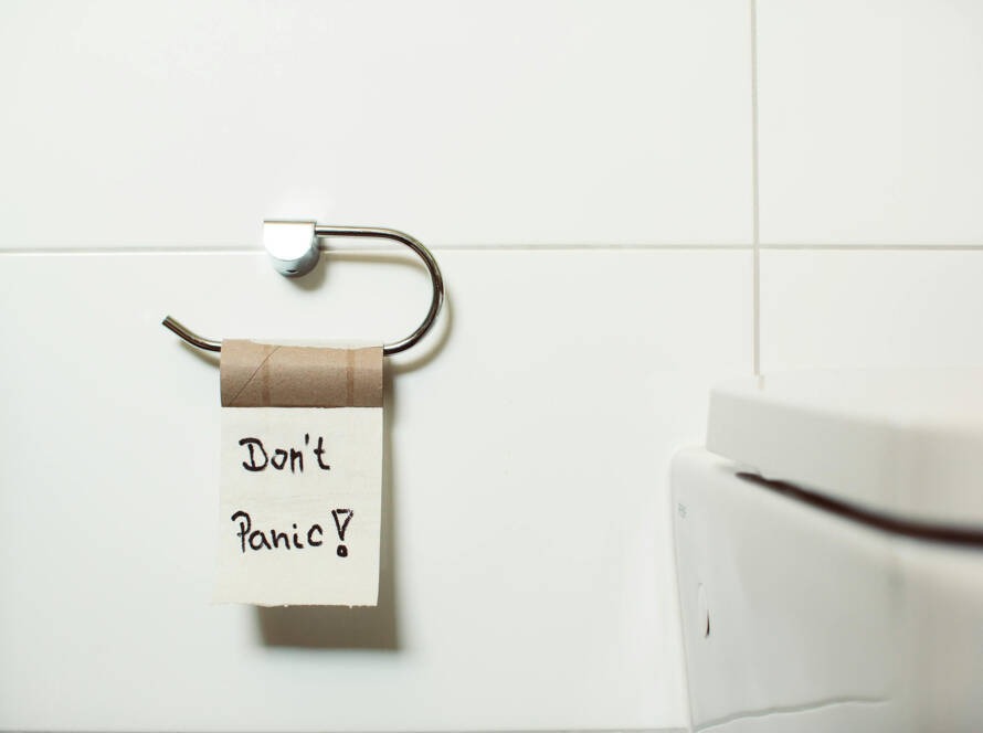 Toilet paper holder with a note reading "Don't Panic!" next to a modern smart toilet in a clean bathroom setting, reflecting the humor and comfort associated with Smart Thrones' innovative bathroom solutions.