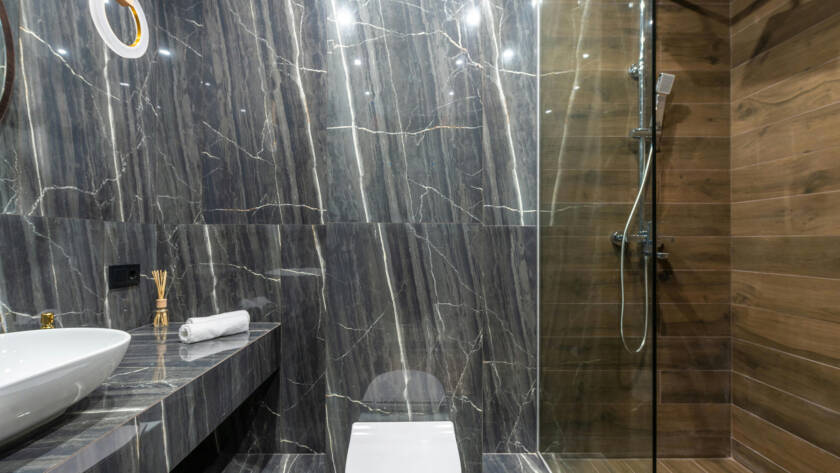 Modern bathroom featuring a smart toilet, elegant marble walls, sleek countertop with a basin, and a glass shower enclosure, emphasizing luxury and hygiene.