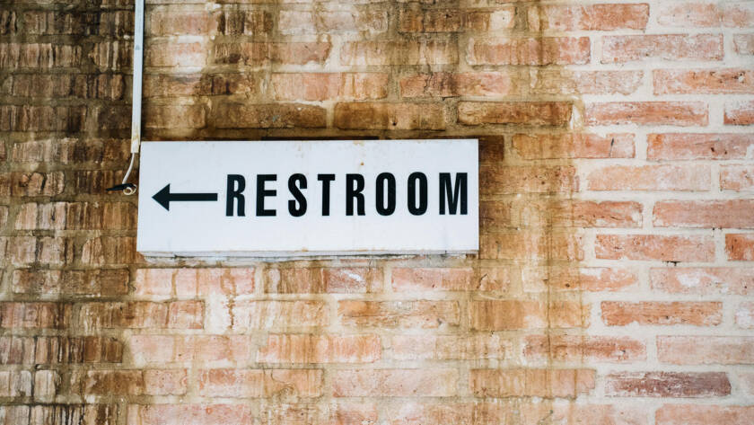 Restroom sign pointing left against a brick wall, indicating location for smart toilet installations.