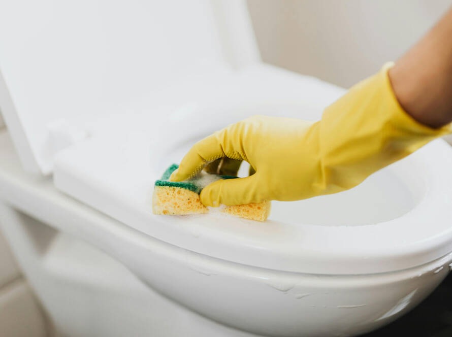 Person cleaning a smart toilet with a sponge and yellow gloves, emphasizing maintenance for modern bathroom upgrades.