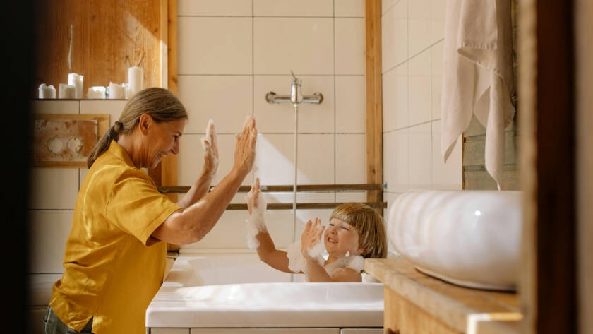 Grandmother and child playing together in a bathtub, enjoying a fun bath time with bubbles in a cozy bathroom setting.
