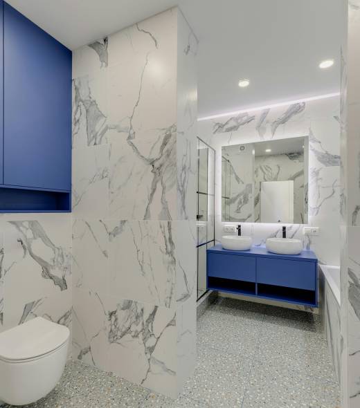 Modern bathroom featuring a smart toilet, sleek blue cabinetry, dual vessel sinks, and marble-patterned walls, emphasizing luxury and functionality in home upgrades.